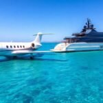 Private jet and luxury yacht in serene waters.
