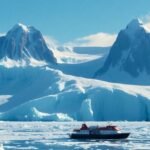 Barco de expedición en un paisaje antártico helado bajo un cielo azul.