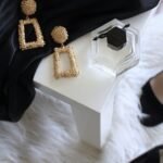 pair of gold-colored earrings on table and black ankle-strap pumps on area rug