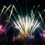 Fireworks explode over a disney castle at night.